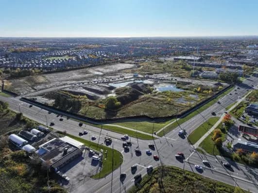 Aerial view of a cleared, hoarded development site beside a major road intersection.