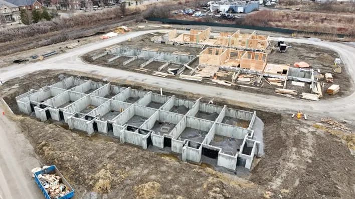 Aerial view of concrete foundation walls in rows, with timber framing started on the block behind.